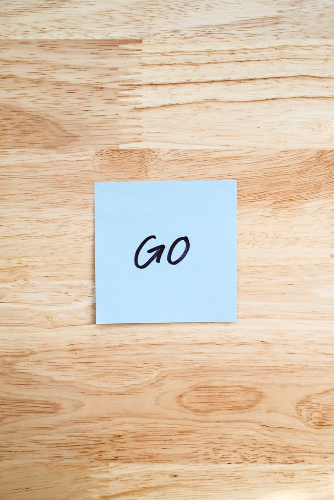 A blue Post-it note labeled 'GO' placed on a light wooden surface.